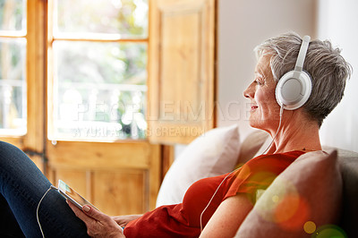 Buy stock photo Shot of a mature woman sitting on her sofa listening to music on a digital tablet