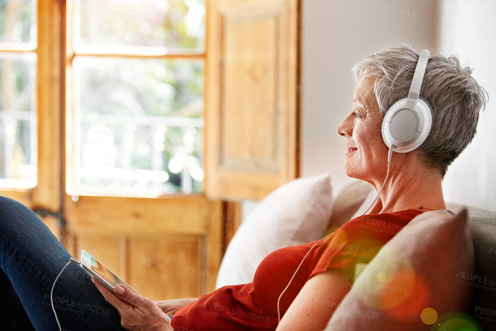 Buy stock photo Shot of a mature woman sitting on her sofa listening to music on a digital tablet