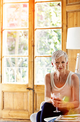 Buy stock photo Portrait of a smiling mature woman relaxing on a chair at home with a glass of wine