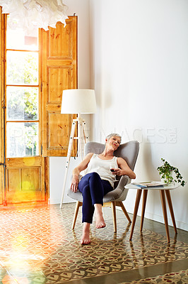 Buy stock photo Shot of a smiling mature woman relaxing on a chair at home with a glass of wine