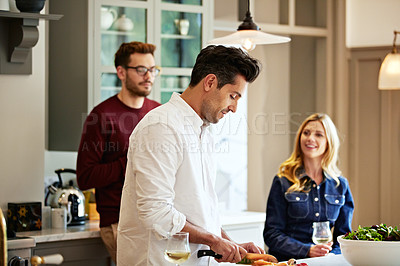 Buy stock photo Shot of a group of friends talking and drinking wine while preparing a meal together