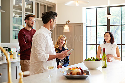 Buy stock photo Shot of a group of friends talking and drinking wine while preparing a meal together