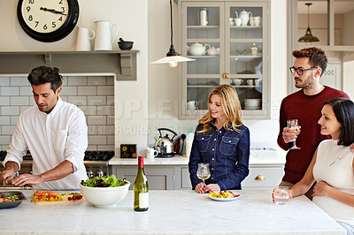 Buy stock photo Shot of a group of friends talking and drinking wine while preparing a meal together