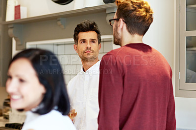 Buy stock photo Shot of two young men drinking wine and talking together in a kitchen at a get-together