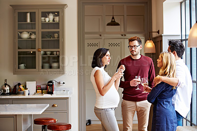 Buy stock photo Shot of a group of friends drinking wine and talking together in a kitchen at a get-together