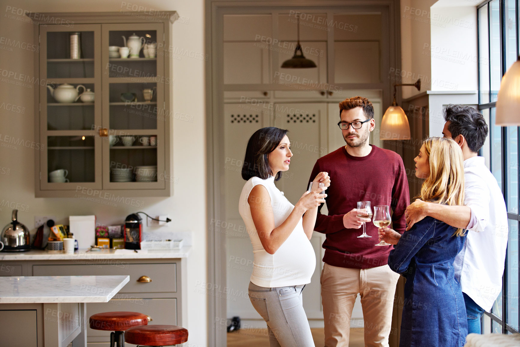 Buy stock photo Shot of a group of friends drinking wine and talking together in a kitchen at a get-together