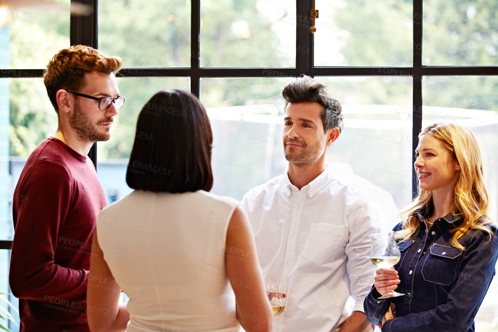 Buy stock photo Shot of a group of friends drinking wine and talking together in a kitchen at a get-together