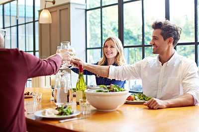 Buy stock photo Shot of a group of friends toasting while enjoying a home-cooked dinner together