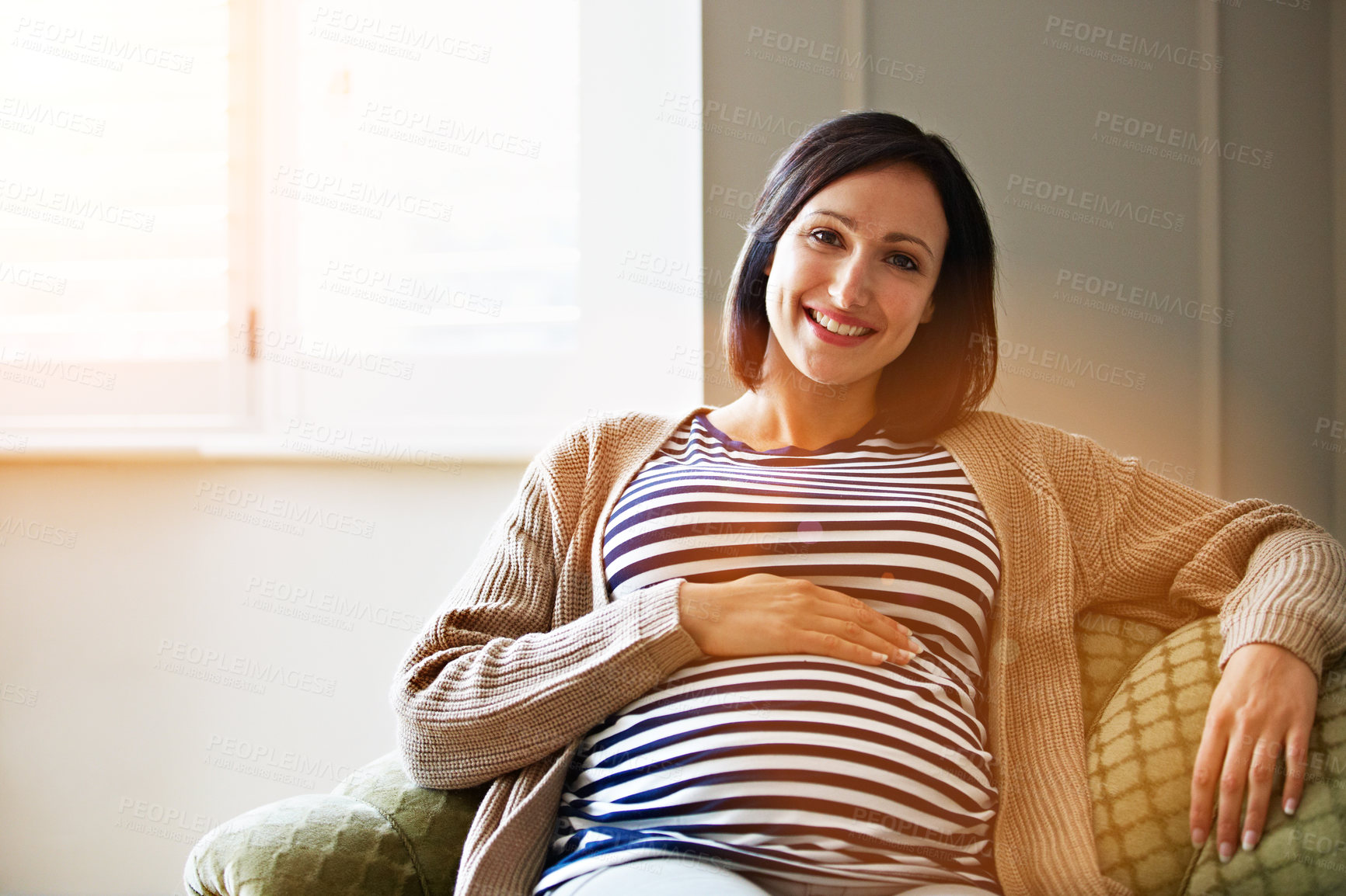 Buy stock photo Portrait of a smiling pregnant woman sitting on her sofa