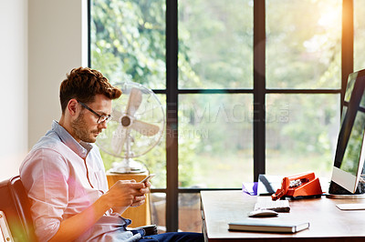 Buy stock photo Shot of a young man sending at text message while sitting in his home office