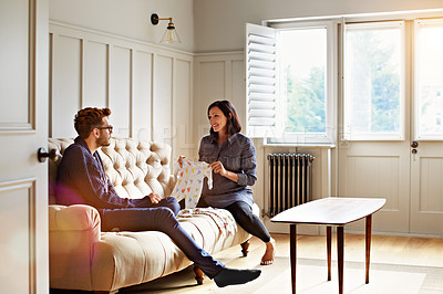 Buy stock photo Shot of a young pregnant woman showing her husband baby clothing while sitting on their sofa