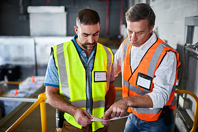 Buy stock photo Shot of two workers discussing paperwork while standing on stairs in a large warehouse
