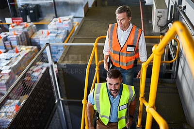 Buy stock photo Shot of two workers walking down stairs in a large warehouse