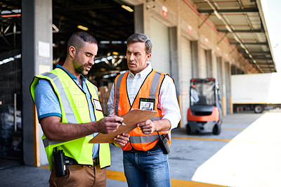 Buy stock photo Shot of two workers talking together over a clipboard while standing at the entrance of a warehouse
