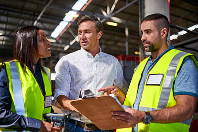 Buy stock photo Shot of a group of coworkers reading paperwork while standing in a large warehouse