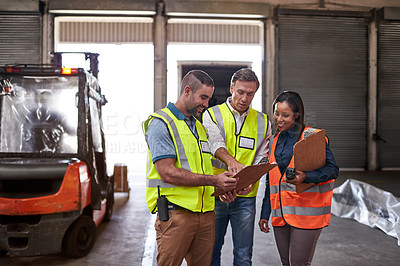 Buy stock photo Shot of a group of coworkers reading paperwork while standing in a large warehouse
