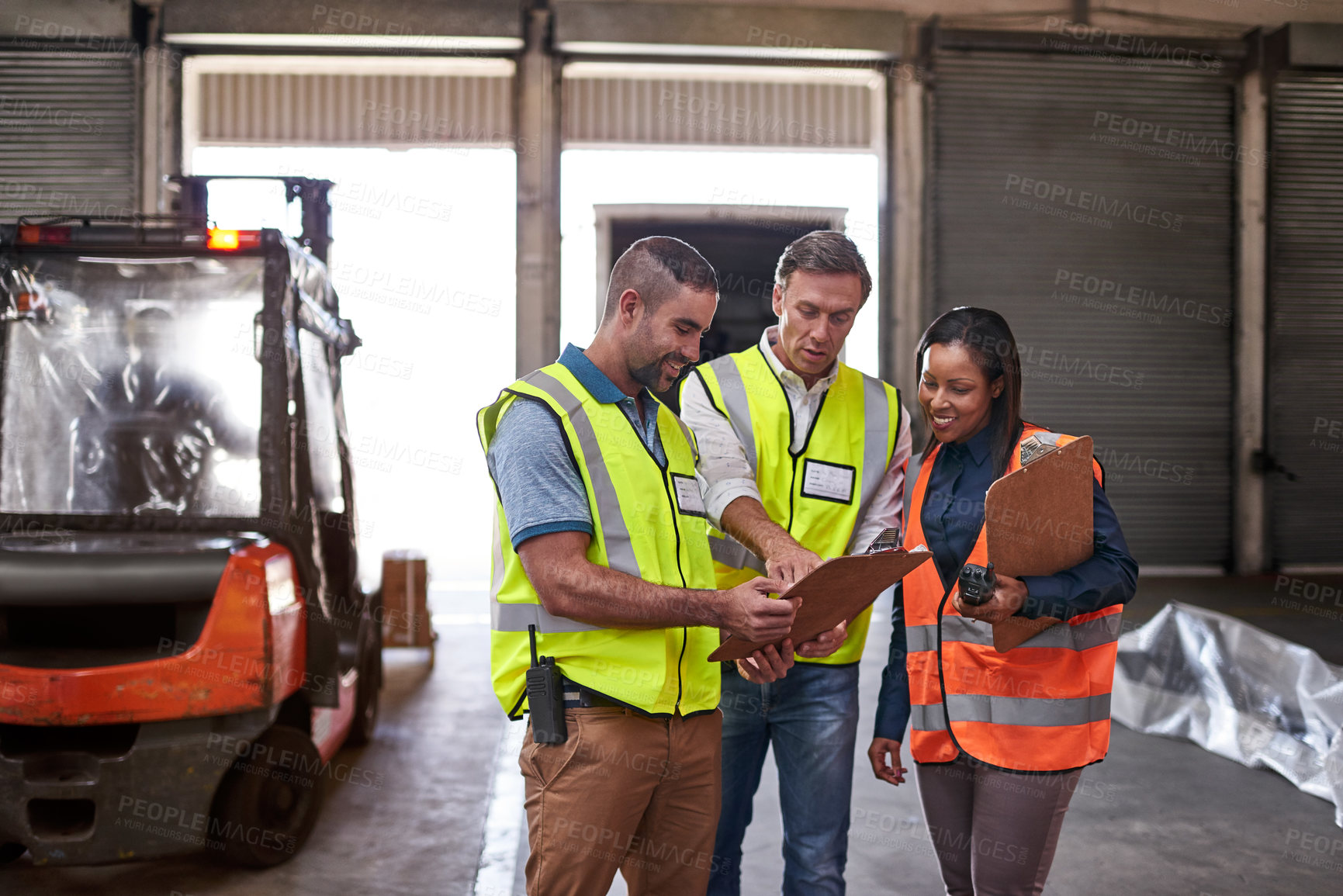 Buy stock photo Shot of a group of coworkers reading paperwork while standing in a large warehouse