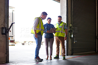 Buy stock photo Shot of three workers talking together inside the entrance to a large warehouse