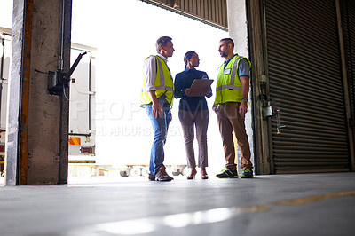 Buy stock photo Shot of three workers talking together inside the entrance to a large warehouse