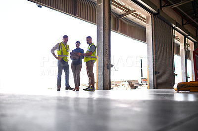 Buy stock photo Shot of three workers talking together inside the entrance to a large warehouse