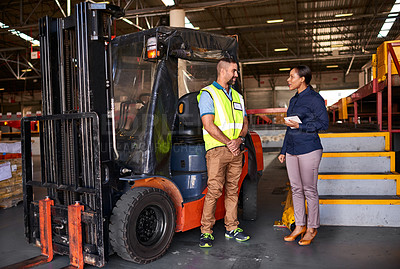 Buy stock photo Shot of two coworkers talking together beside a forklift while standing in a large warehouse