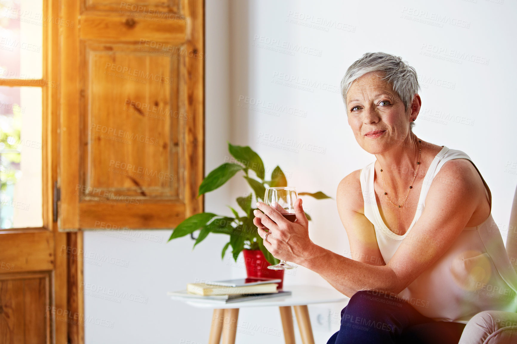 Buy stock photo Portrait of a smiling mature woman relaxing on a chair at home with a glass of wine