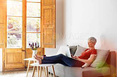 Buy stock photo Shot of a mature woman relaxing on her sofa at home using a laptop