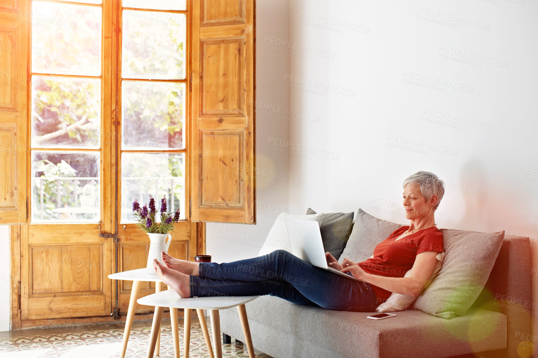 Buy stock photo Shot of a mature woman relaxing on her sofa at home using a laptop