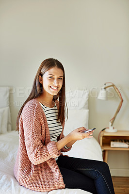 Buy stock photo Portrait of a smiling young woman sitting on her bed using a cellphone