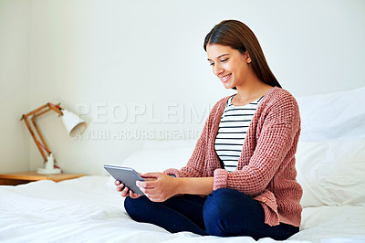 Buy stock photo Shot of a young woman sitting on her bed using a digital tablet