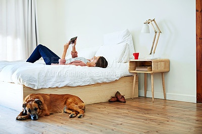Buy stock photo Shot of a young woman lying on her bed using a digital tablet