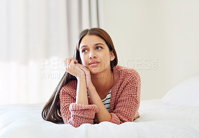 Buy stock photo Shot of a young woman lying on her bed deep in thought