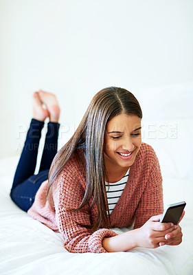 Buy stock photo Shot of a young woman lying on her bed using a cellphone