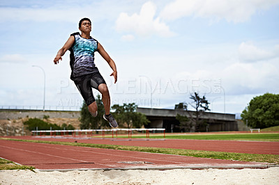 Buy stock photo Shot of a young woman in mid air doing a long jump on a sports field