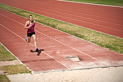Buy stock photo Shot of a young man running down a track to do a long jump on a sports field