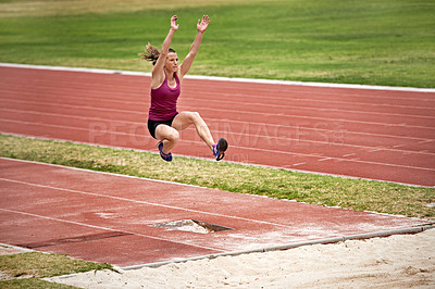 Buy stock photo Shot of a young woman in mid air doing a long jump on a sports field