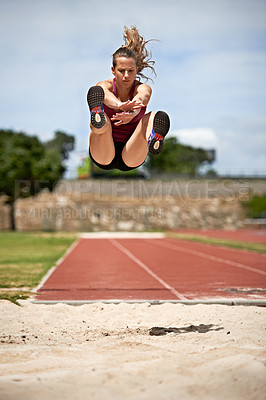 Buy stock photo Shot of a young woman in mid air doing a long jump on a sports field