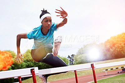 Buy stock photo Shot of a young woman in mid air while jumping over a hurdle on a sports field