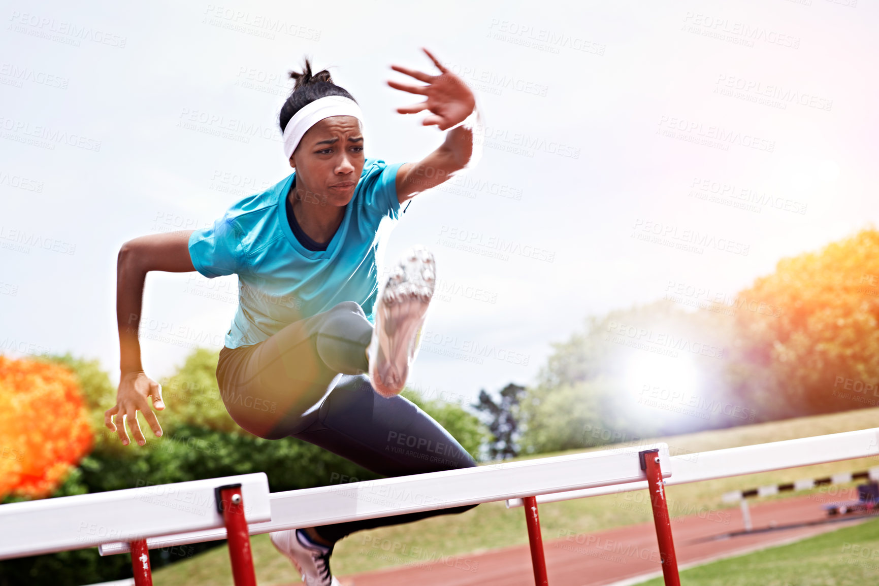 Buy stock photo Shot of a young woman in mid air while jumping over a hurdle on a sports field