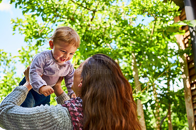 Buy stock photo Shot of a mother holding her smiling baby girl up in the air outdoors