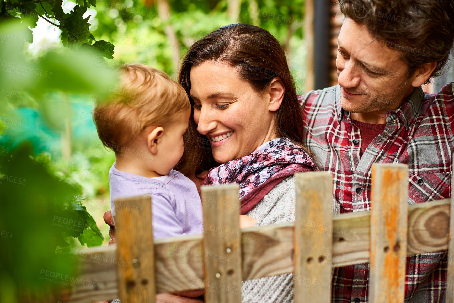 Buy stock photo Shot of a couple with their baby girl standing their organic garden