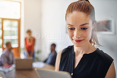 Buy stock photo Shot of a smiling young woman using a digital tablet in an office with colleagues in the background