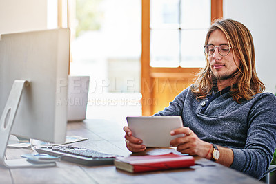 Buy stock photo Shot of a young man using a digital tablet while sitting at his desk in an office