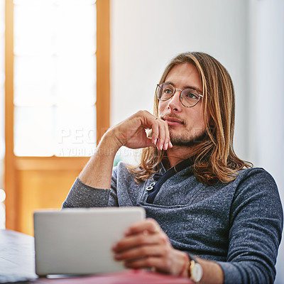 Buy stock photo Shot of a young man deep in thought while using a digital tablet at his desk in an office