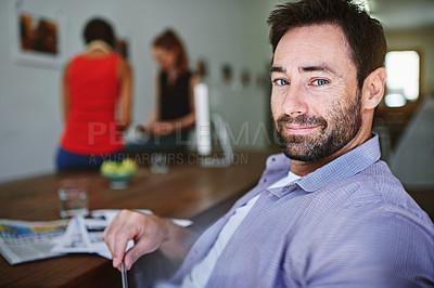 Buy stock photo Portrait of a smiling man sitting at a desk in an office with colleagues working in the background