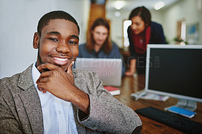 Buy stock photo Portrait of a smiling young man sitting at a desk in an office with colleagues working in the background