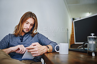 Buy stock photo Shot of a young man using a digital tablet while sitting at his desk in an office