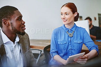 Buy stock photo Shot of two smiling colleagues talking together while while using a digital tablet in an office