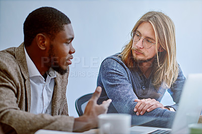Buy stock photo Shot of two young colleagues talking together while working on a laptop at a desk in an office