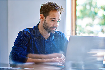 Buy stock photo Shot of a man sitting at a desk in an office working on a laptop